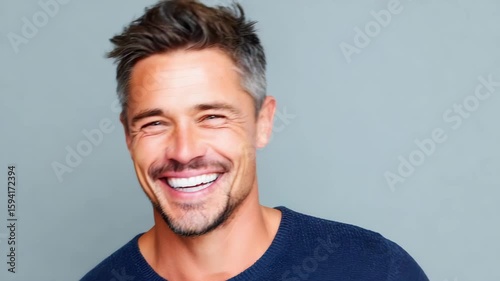 Smiling man with levity and laughter shows happiness and joy wearing blue sweater with short hair and facial hair gray joyful