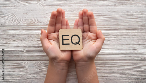 Child Hands Holding Wooden Block with EQ Text on White Wooden Background Emotional Intelligence