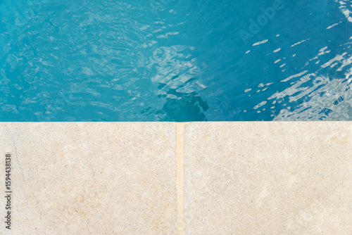 Gros plan sur l’eau cristalline d’une piscine avec aperçu du contour en pierre naturelle, illustrant un travail soigné par une entreprise spécialisée.