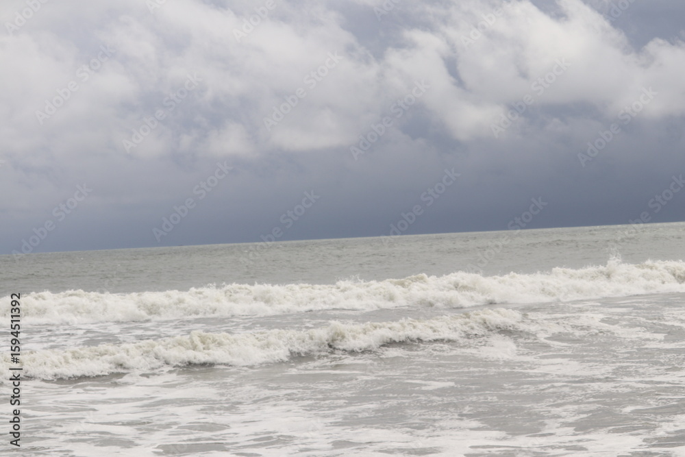Obraz premium Crashing Waves Under a Cloudy Sky Creating Beautiful Ocean Foam Patterns