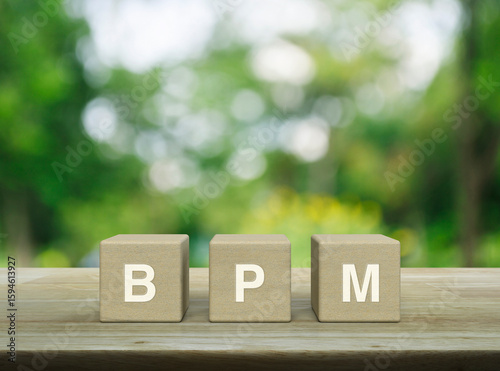 BPM acronym on wood block cubes on wooden table over blur green tree in park, Business process management concept