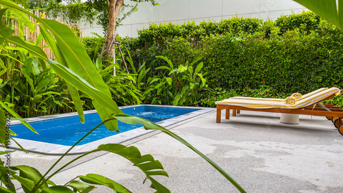 Pool chairs and beautiful blue water with green tree in the background.