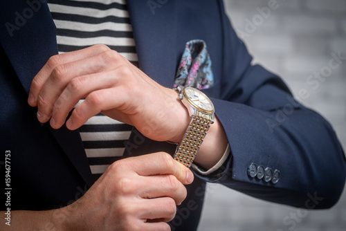 Elegant man putting a gold watch on his wrist. Luxury, style, and time management concept. Close-up of male hands with premium accessories