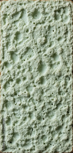 Macro texture of a worn, pale sage green sponge with uneven pores, an abstract background.