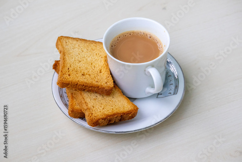 Fotografija Steaming hot milk tea with delightful bubbles and crunchy rusk biscuits artfully arranged on a wooden backdrop