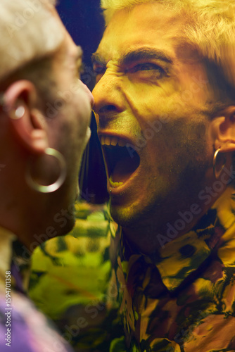Enraged young male with earring yelling in dissatisfaction at reflection on dichroic film