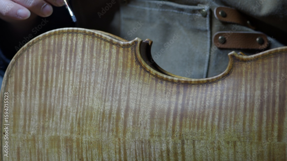 Obraz premium Skilled craftsman applying traditional varnish technique with delicate brush strokes, creating vintage patina on handmade violin surface, enhancing instrument's refined musical character
