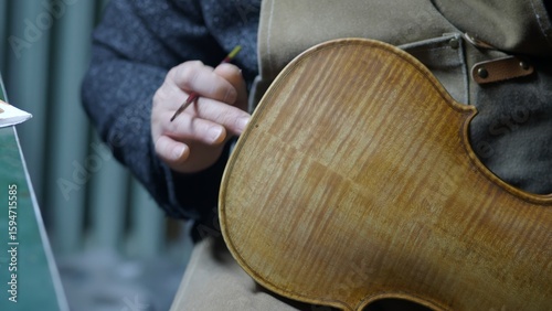Fotografie Skilled luthier carefully applying varnish to handcrafted violin, using traditio