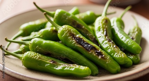 A plate of blistered Shishito peppers, some with charred spots, arranged closely together.