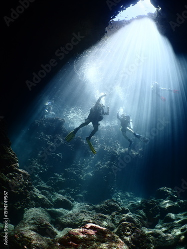 scuba divers in cave coming up to the surface with sun beams and rays