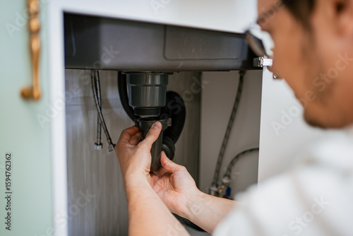 Tableau sur toile Professional plumber working diligently on installing a siphon beneath the kitch