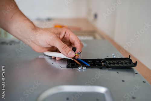 Professional electrician wiring terminal block of electric stove, connecting cables carefully during kitchen renovation process, maintaining electrical safety standards
