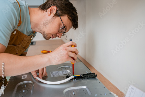 Professional electrician connecting wires and using a screwdriver while installing a new electric stove in a contemporary kitchen, showcasing expertise in appliance installation