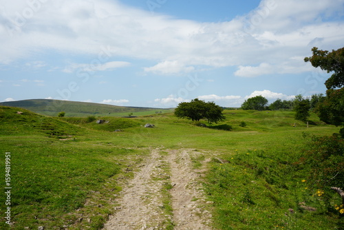 Scenic view of a grassy trail winding through rolling hills under a blue sky at Solomons Temple in The Peak District, England.