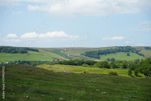 Scenic view of rolling green hills with a winding path under a blue sky at Solomons Temple, The Peak District, England.