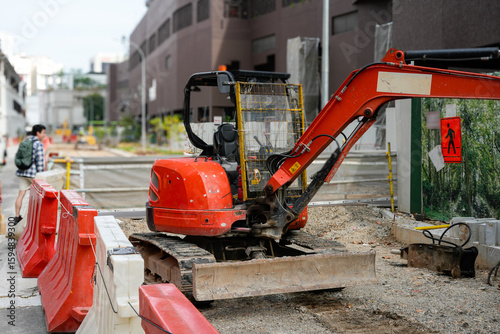 Fototapeta Naklejka Na Ścianę i Meble -  A compact orange mini excavator is parked on a construction site in an urban area