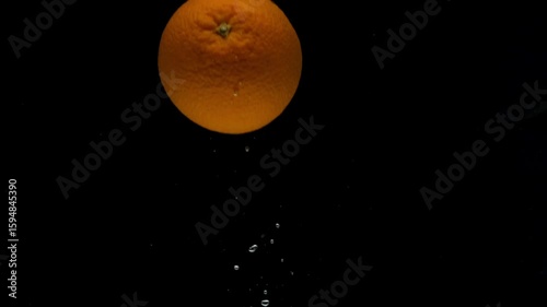 Slow motion one orange falling into transparent water on black background. Fresh citrus splashing in aquarium. Fruits, food