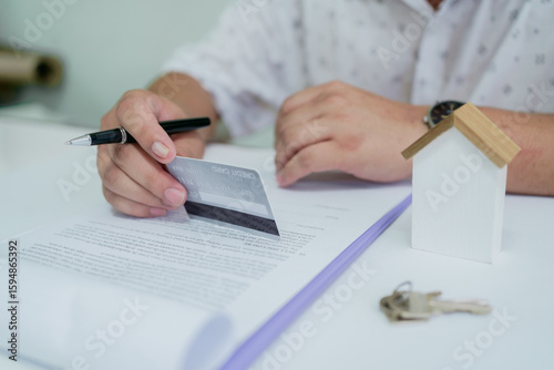 Businessperson signing real estate contract while holding credit card, representing property agreement, mortgage, rent, or house buying process.