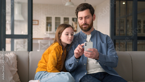 Positive joyful happy Caucasian family dad parent guy father celebrating man daughter win male using mobile phone success little child girl kid rejoicing victory online game victory cellphone at home