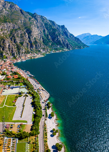 Aerial view of Limone sul Garda, a colorful lakeside town in Italy nestled between Lake Garda and steep mountains under a bright blue sky
