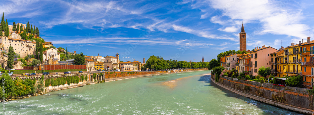 Fototapeta premium View of Ponte Pietra, Verona’s ancient Roman stone bridge crossing the Adige River under a clear sunny sky with historic buildings nearby