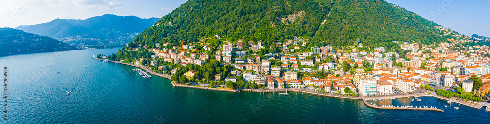 Fototapeta premium Aerial summer view of Lake Como with deep blue water, surrounding green hills, villas, and boats under a clear, sunny sky in Italy
