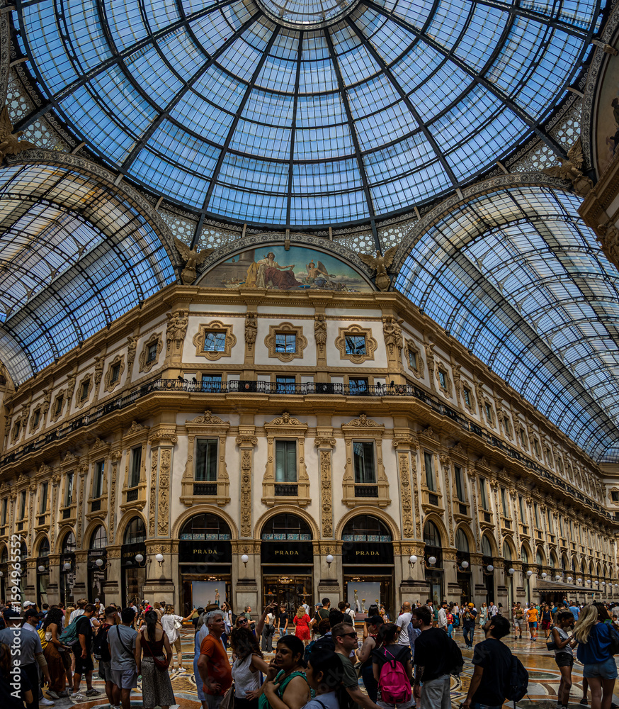 Naklejka premium Interior view of Galleria Vittorio Emanuele II in Milan with glass dome, ornate facades, and decorative fresco under bright daylight
