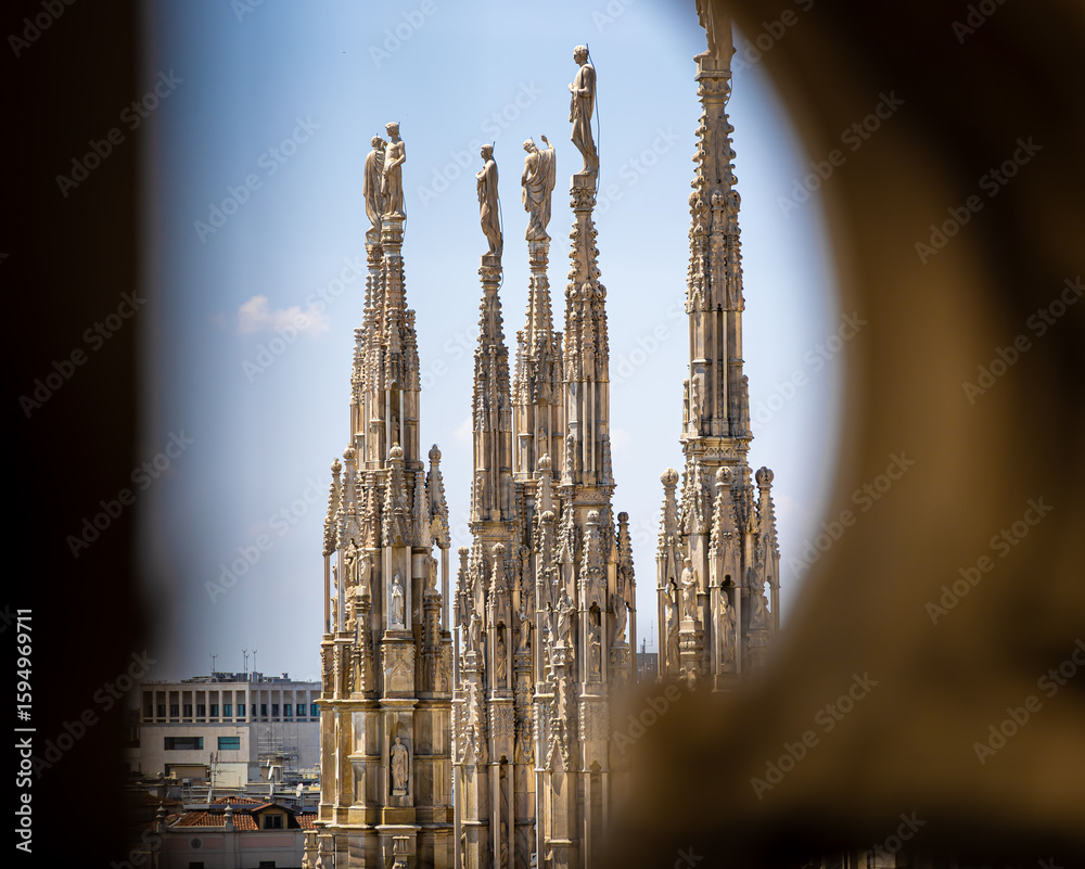 Gothic-style Milan Cathedral facade with ornate spires and intricate stonework against clear blue sky, captured in daylight Gothic-style Milan Cathedral facade with ornate spires and intricate stonework against clear blue sky, captured in daylight