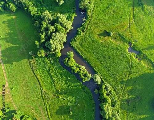 Fotografie River flowing through lush green meadows and forests from an aerial perspective