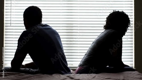 A couple quarreling concept of family relationship problems divorce, black silhouette of man and woman sitting at bed back to back resentment towards each other window in dark room