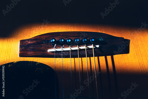 Acoustic guitar bridge and strings. Wooden guitar bridge, with strings and tuning pegs in sharp focus, revealing the craftsmanship of the instrument