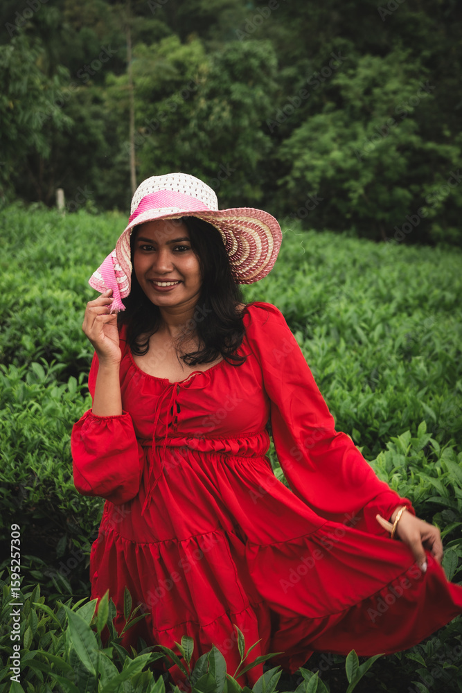 Obraz premium A woman in a stylish sunhat and red dress enjoys a serene moment in a lush tea plantation, surrounded by rolling green hills and nature.