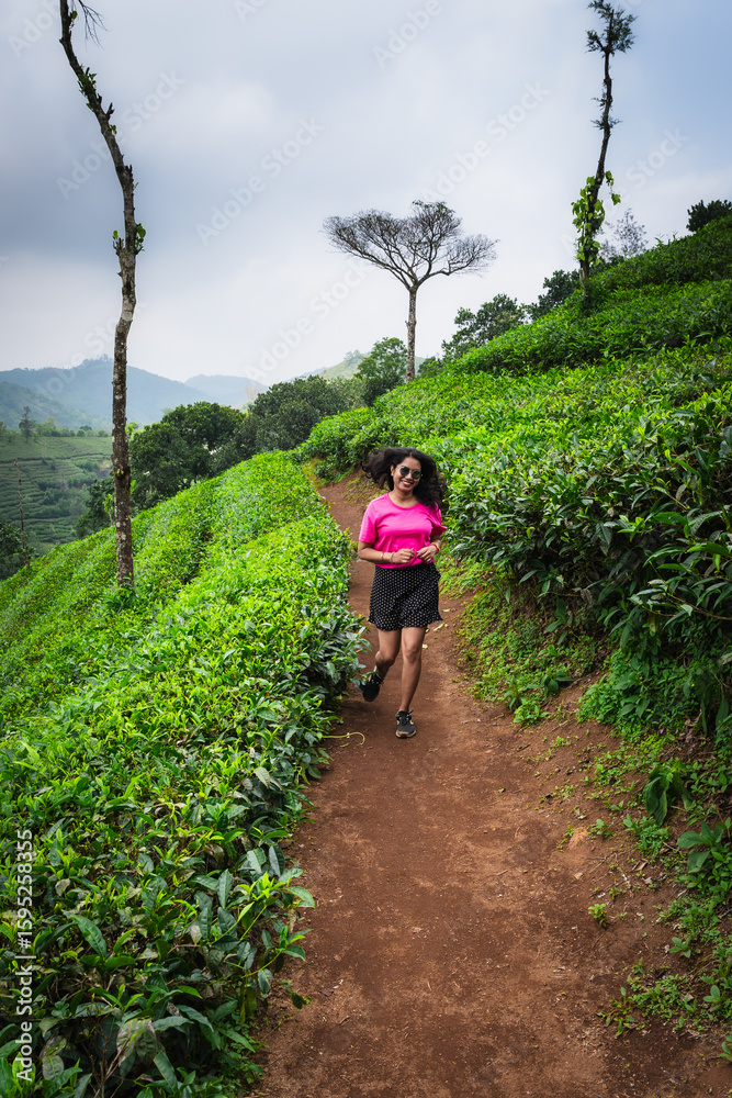Obraz premium Young Indian woman running through the scenic tea plantations of Kerala, embracing fitness and adventure amidst nature