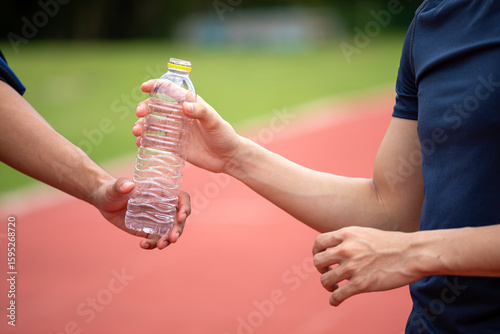 Konstfotografi Close-up of two athletes hands exchanging a plastic water bottle on outdoor runn