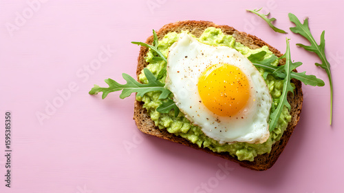 Deliciously healthy avocado toast topped with a perfectly fried egg and fresh greens on a pink background