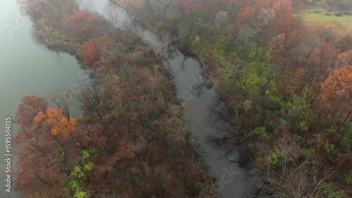 Aerial footage of forested land near Jackson Michigan on a foggy day in late autumn. The grand river snaking through colorful trees