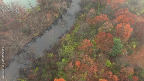 Aerial footage of forested land near Jackson Michigan on a foggy day in late autumn. The grand river snaking through colorful trees
