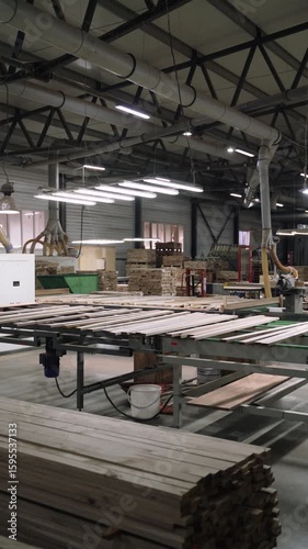 Vertical video showing an automated wood processing line in a spacious, modern woodworking factory. Wooden planks move along a conveyor system, surrounded by industrial machines.