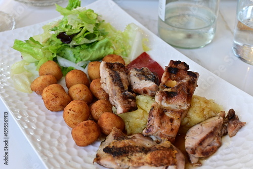 Plato de pollo asado en trozos con croquetas, ensalada de lechuga, puré de patatas y pimiento rojo
