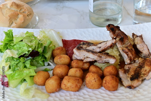 Plato de pollo asado en trozos con croquetas, ensalada de lechuga, puré de patatas y pimiento rojo