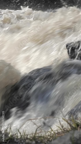 A riverside grassy rock with a rapid river flowing by it. Geology shot with the camera very slightly moving upwards. Selective focus. Vertical video.