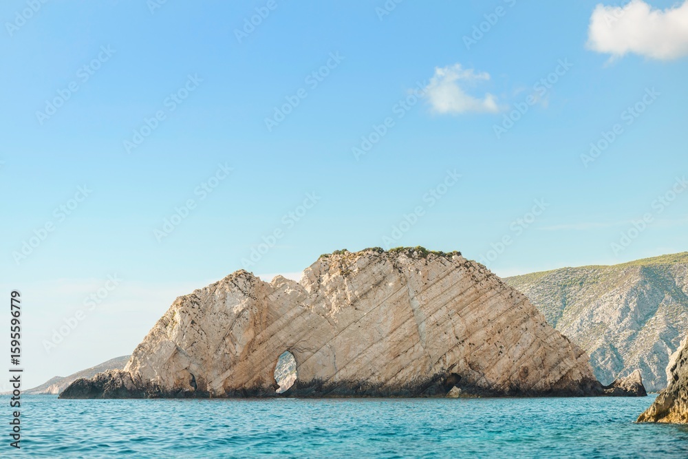 Fototapeta premium A rock island formation with a unique natural arch, set against the azure Aegean Sea and sky, creates a picturesque view in Greece