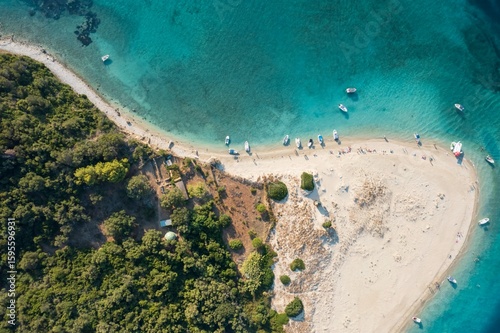Photography An aerial perspective reveals a picturesque sandy beach in Greece, dotted with sunbathers and boats along the shore
