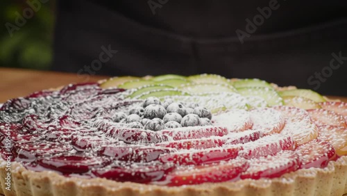 Powdered sugar being sprinkled on a colorful fruit tart with blueberries and sliced fruits