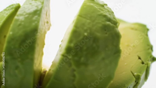 Close up of sliced avocado pieces stacked together on a white surface in bright lighting