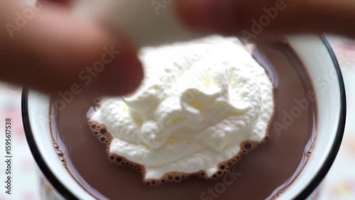 Close up of a cup of chocolate pudding with whipped cream being added on top in a white cup