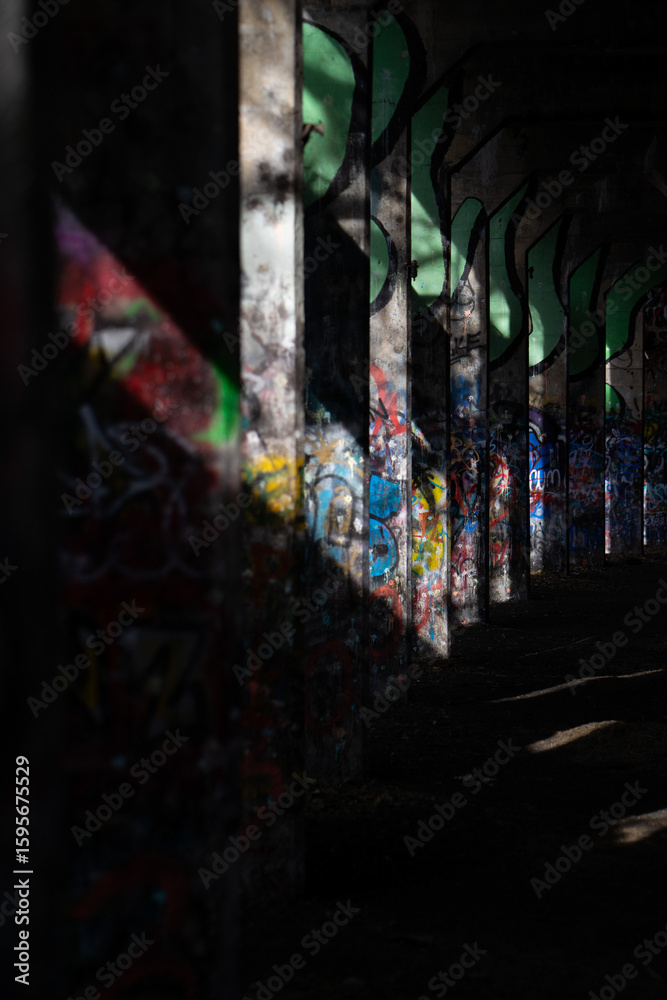 Fototapeta premium Graffiti-covered concrete pillars in abandoned underpass with dramatic light