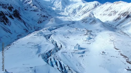An aweinspiring aerial view captures ancient monasteries nestled amidst a vast, snowcovered mountain range with a dramatic glacier carving through the landscape