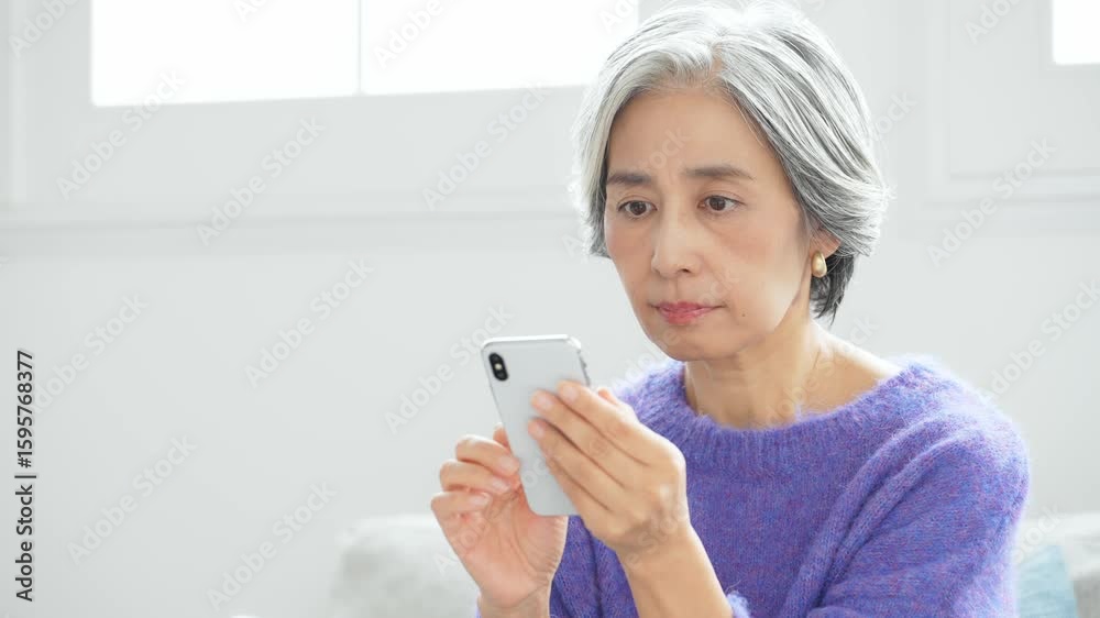 リビングルームでスマホを使うシニア女性 リビングルームでスマホを使うシニア女性