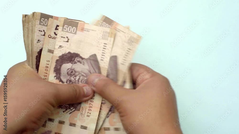 A person's hands count a stack of 500 Mexican Pesos banknotes against a plain background, symbolizing finance, commerce, and cash transactions in the mexico economy